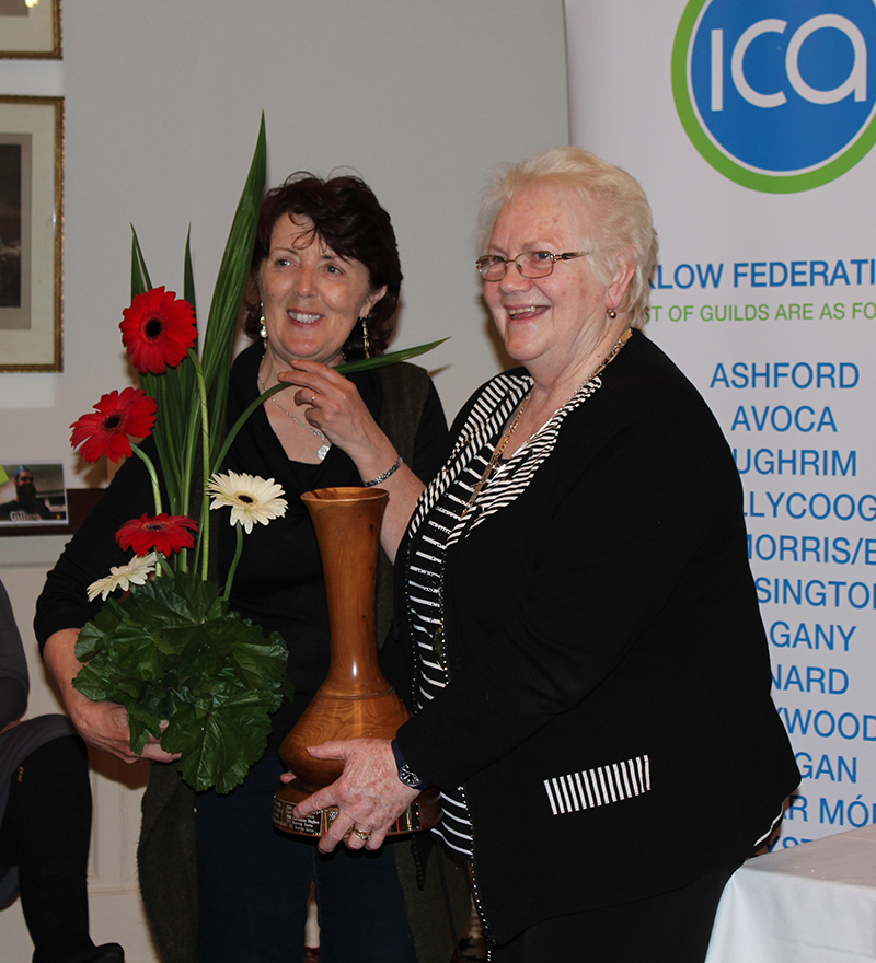 Christina holds her flower arrangement with Madge Kenny, Wicklow Federation President holding the Tinahely Show Cup, a large wooden vase.